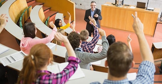 Professor and students in a classroom, students raising hands