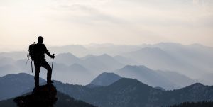 Silhouette of man standing on mountain peak in the early morning looking at mountain range below