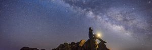 person sitting on rock looking up at the night sky at the galaxy