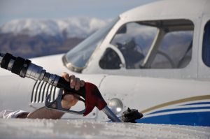 up close photo of person filling small airplane with fuel and mountains in the background