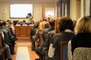 men and women sitting in meeting room facing a commission of local government officials at the front of the room