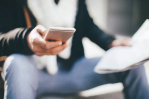 Man sitting on the stairs, reading newspaper and using his smart phone