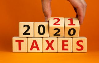 Business concept of planning 2021. Male hand flips wooden cubes and changes the inscription 'Taxes 2020' to 'Taxes 2021'. Beautiful orange background, copy space.