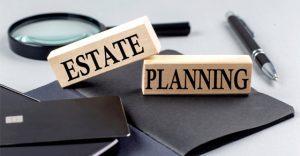 stacked wood blocks with words Estate Planning in text, sitting on desk with notepad, pen and magnifying glass