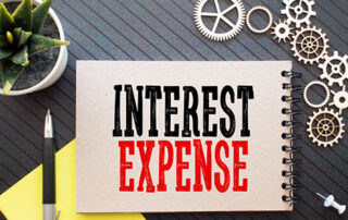 Sat on a table | A aloe plant in a pot to the left corner | On the right nine gears | a push pin at the bottom of the gears | a notebook in the center | written on the notebook in big letter is Interest Expense | left of the notebook is a pen on top of a piece of paper | DWC CPAs and Advisors | business consulting, tax services, audit and assurance, estate and gift planning, wealth management, bookkeeping, outsourced accounting | Grand Junction CO | Montrose CO | Glenwood Springs CO | One Big Beautiful Bill Act (OBBBA)