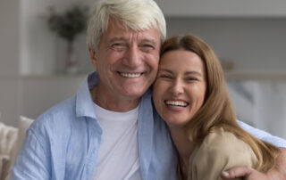 A women hugging her elderly father | They are both smiling| Sitting on a couch