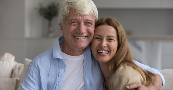 A women hugging her elderly father | They are both smiling| Sitting on a couch